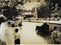 An old image showing children standing at edge of lake, duck houses in centre of water.l 